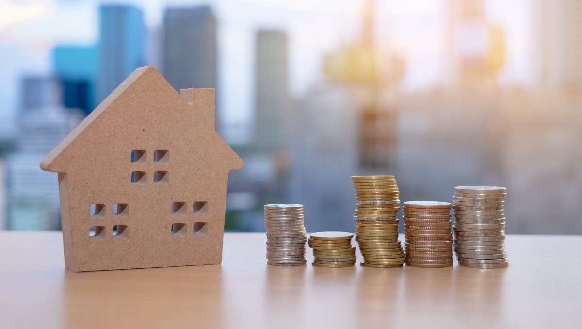 comment bien investir dans l'immobilier – Une pile de pièces et une maison en bois
