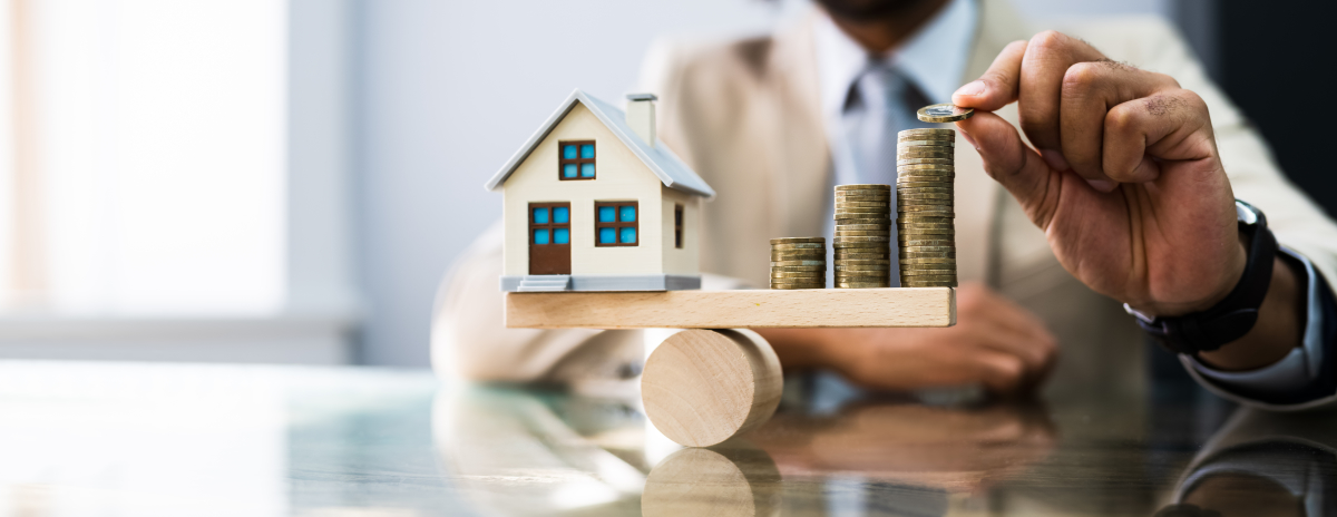  Petite maison en bois en équilibre sur une balance face à des pièces de monnaie