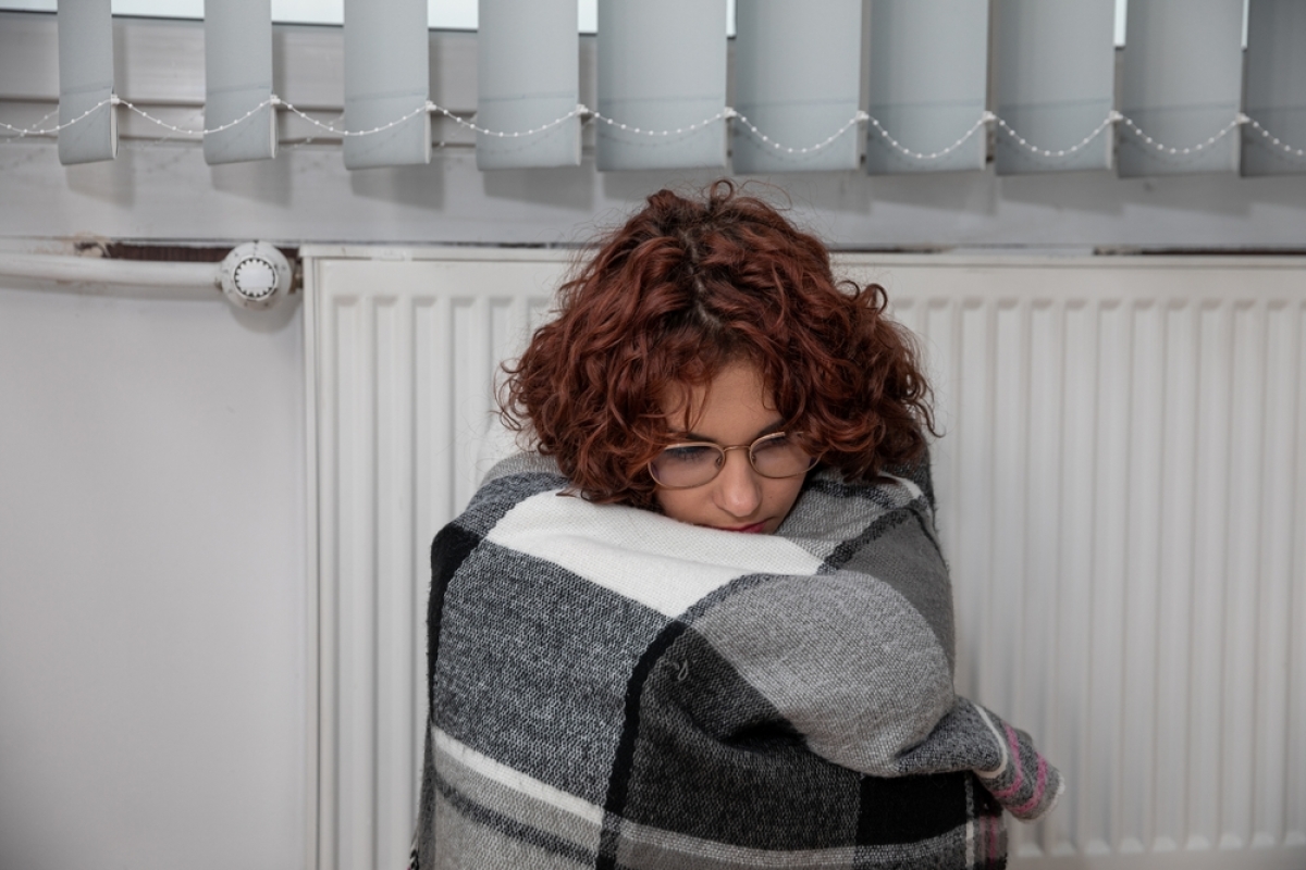 diagnostic de performance énergétique – une jeune femme emmitouflée dans une couverture contre un radiateur