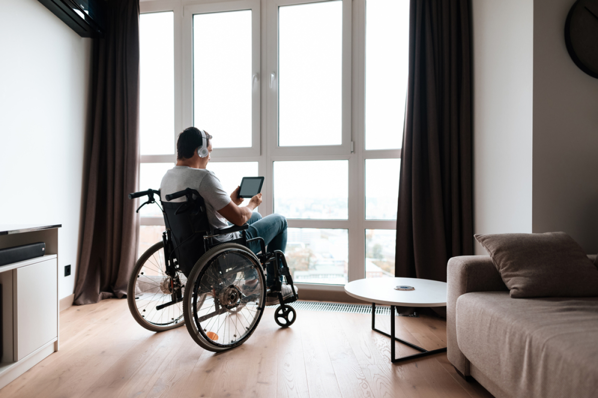 normes PMR logements neufs – une personne à mobilité réduite écoute la musique dans son appartement devant sa fenêtre